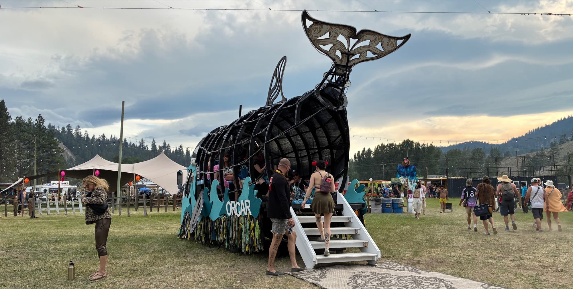 Festival-goers climbing the stairs into the Orcar's open steel body, its carved tail raised against an evening sky