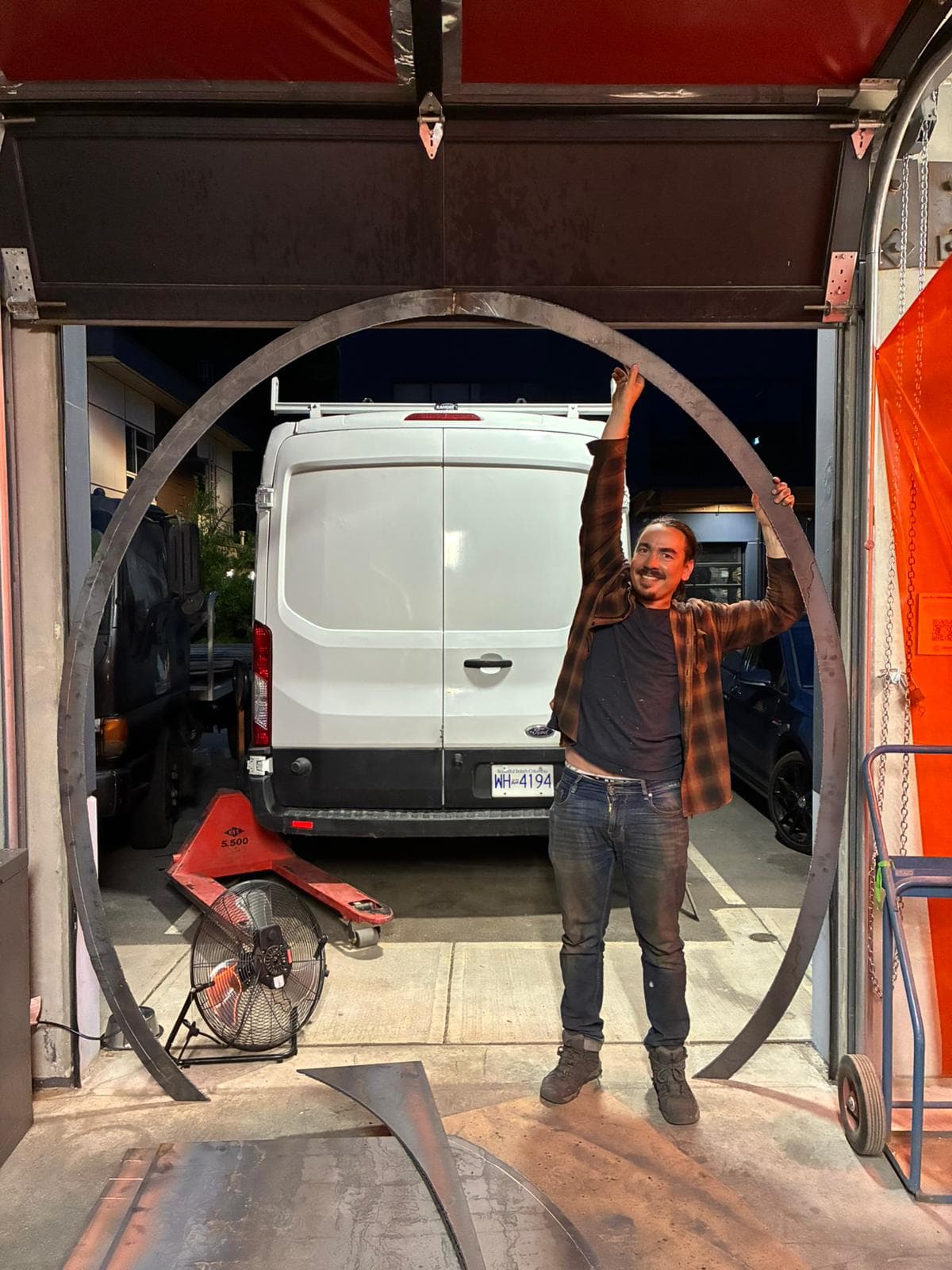 A builder holds up a large steel armature ring at Create Makerspace, part of the Orcar's structural skeleton